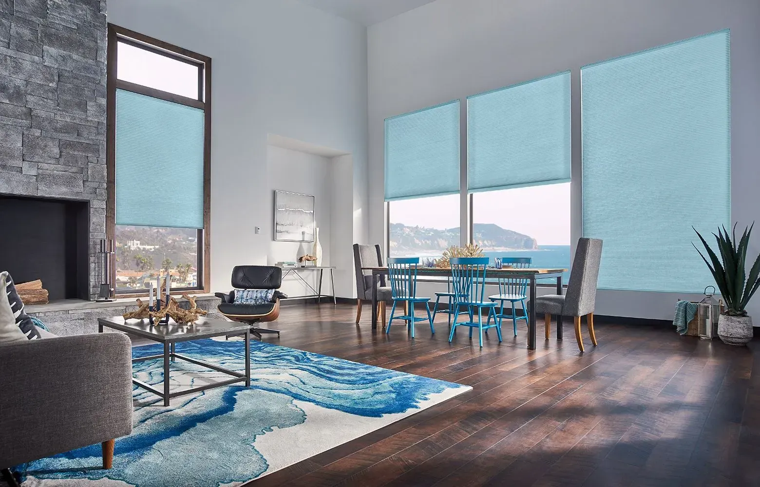 Living room with large windows, blue shades, dining table, and ocean view.