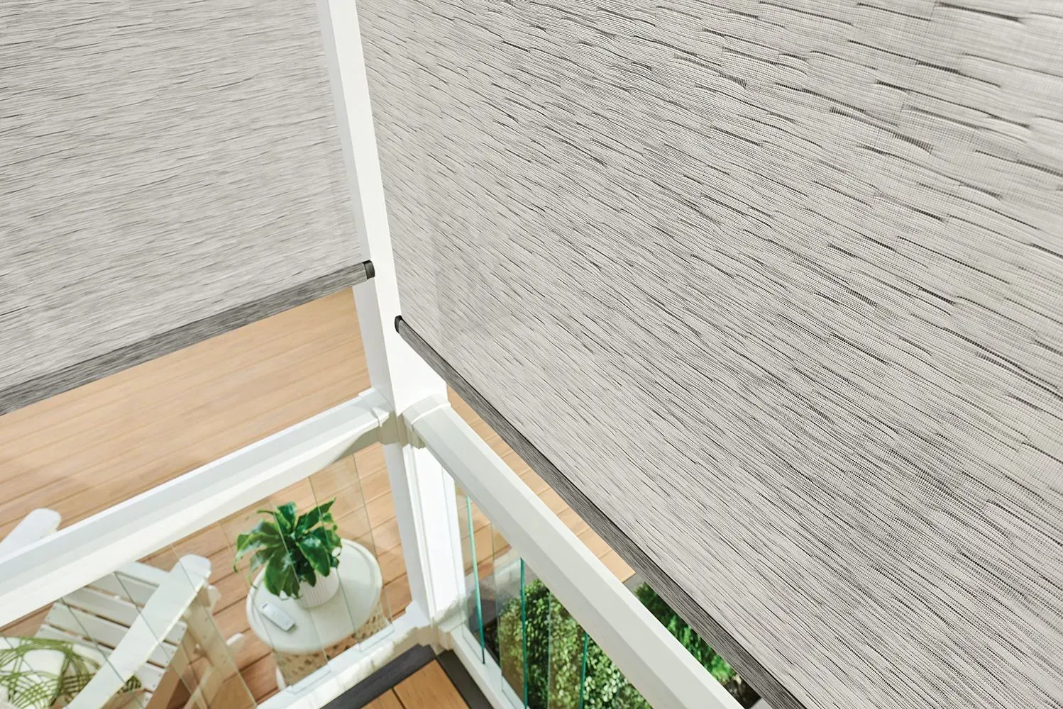 Roller shades on a balcony, casting light shadow. White railing, green plants, and a small table visible below.