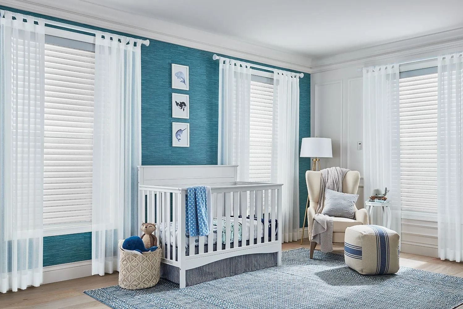 Nursery with white crib, blue accent wall, sheer white curtains, rug, and armchair.