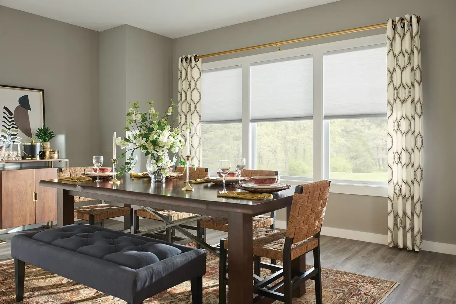 Dining room with a table set for a meal, a bench, chairs, and window with shades and patterned curtains.