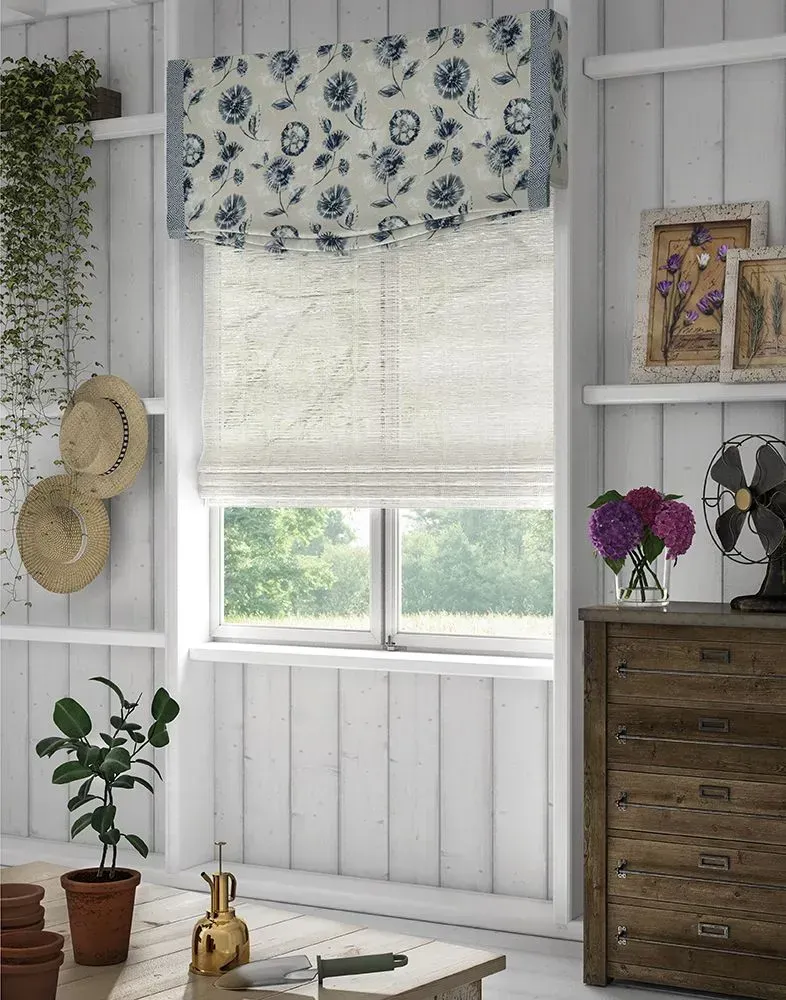White-walled sunroom with floral shade, window, and wood dresser. Plants and hats hang near a window with an outdoor view.