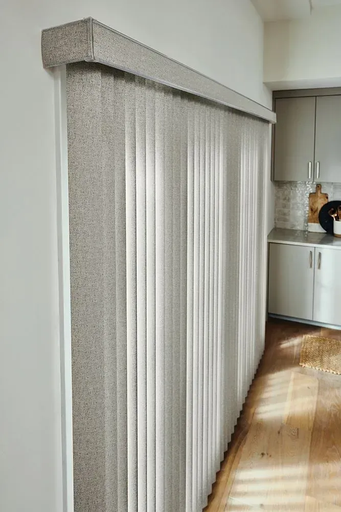 Vertical blinds covering a doorway or large window in a kitchen, with a light-colored speckled valance.