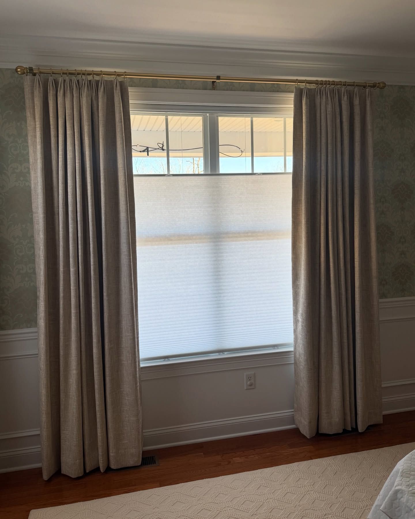 Window with beige curtains and a white cellular shade. Sunlight streams through.