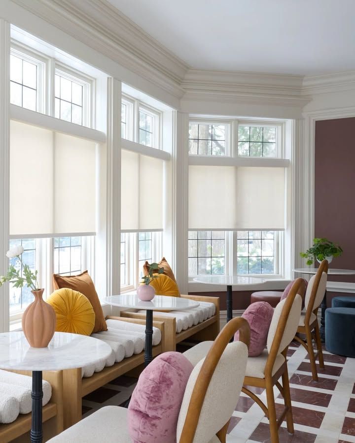 Bright sunroom with seating, large windows, and colorful pillows.
