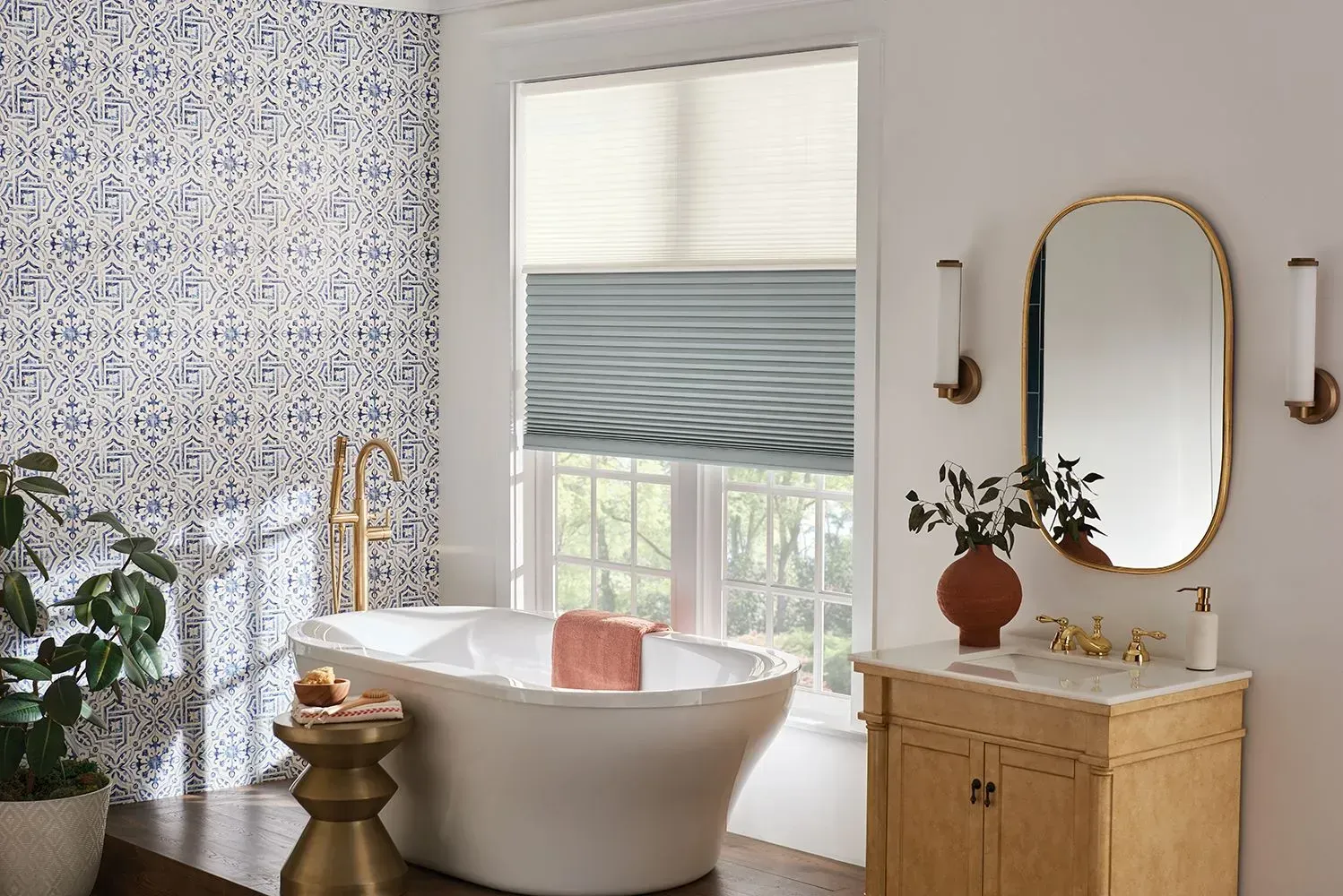 Bathroom with blue patterned tile, white tub, gold fixtures, and beige window shades.