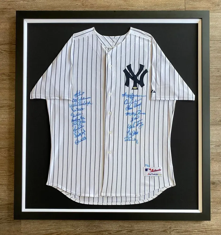 Framed New York Yankees jersey, white with navy pinstripes and team logo, signed in blue, displayed on black mat.