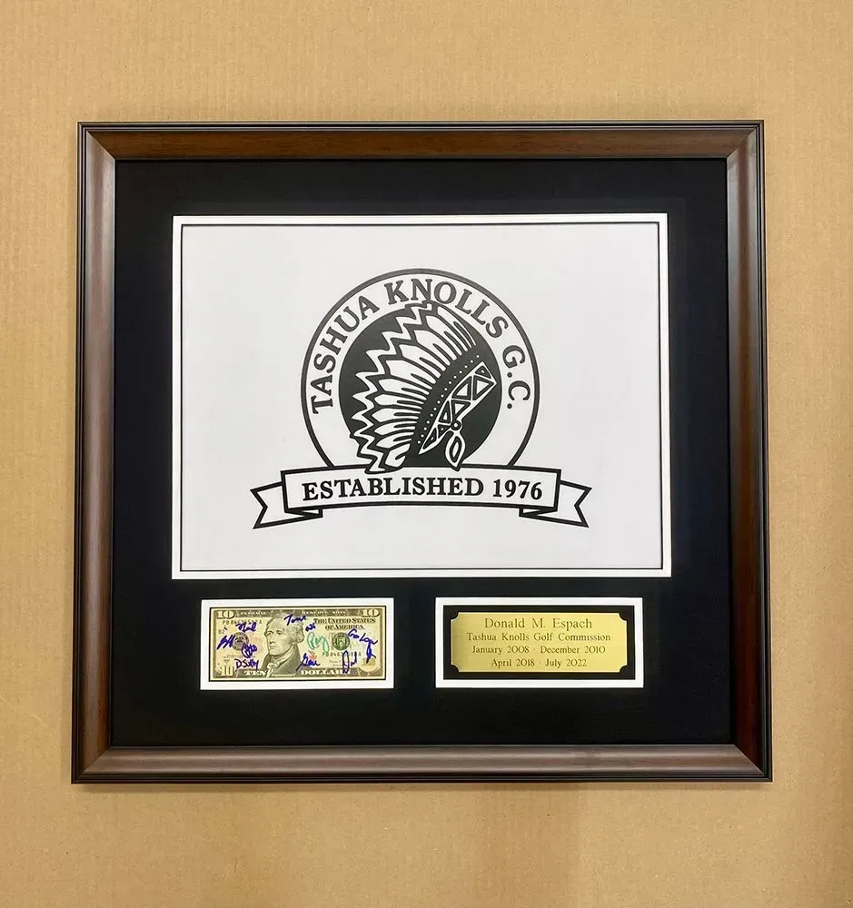 Framed Tashua Knolls G.C. logo with two mounted items below: stamps and a plaque.