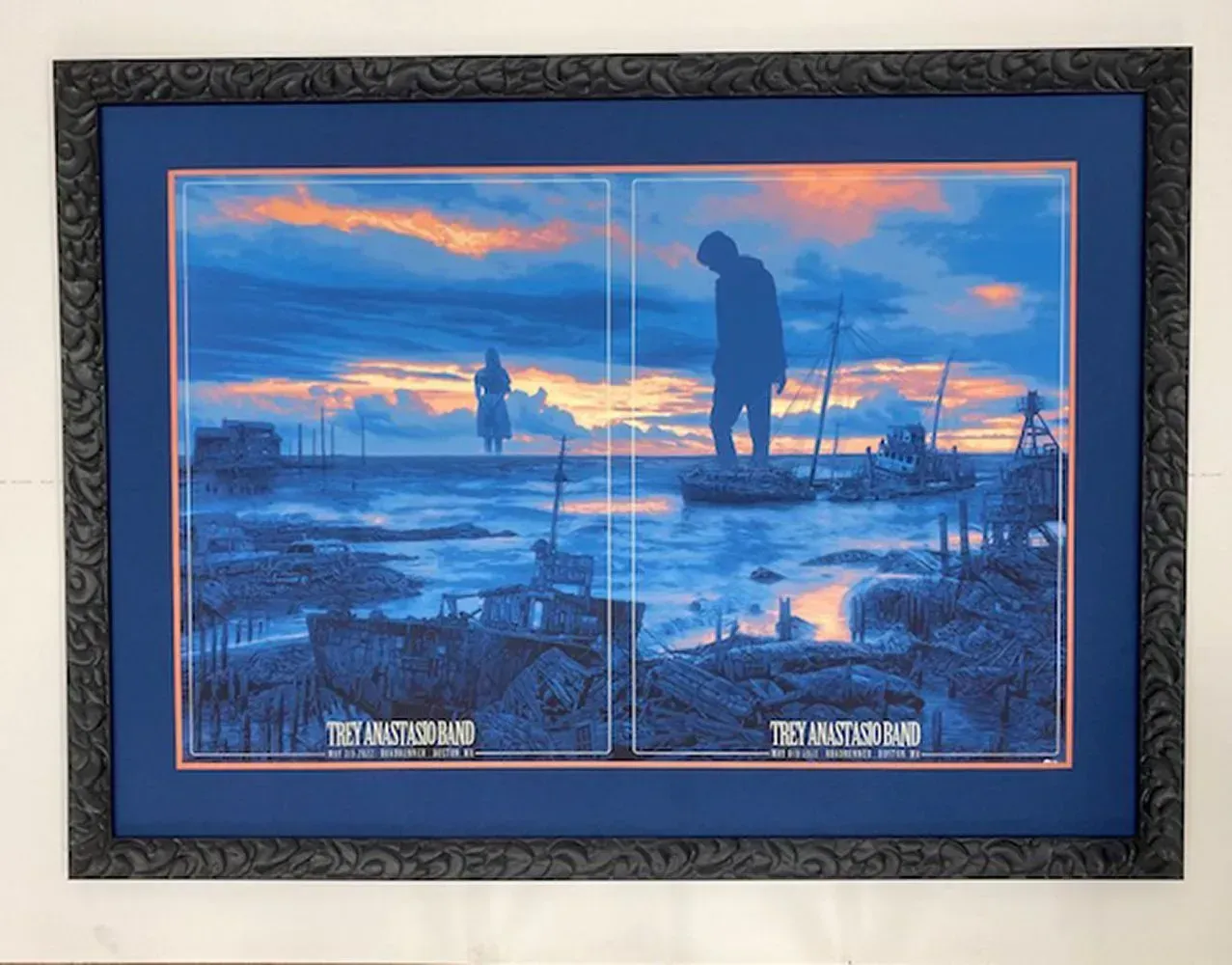Framed concert poster with a blue ocean scene and silhouettes of figures; sunset sky.