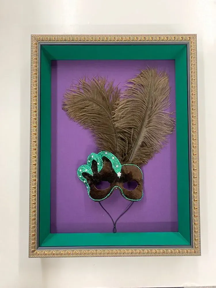 Mardi Gras mask with feathers in a decorative framed box; purple background, green and gold frame.