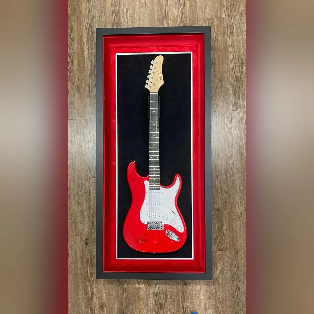 Red guitar in a black framed display case with a red backing.
