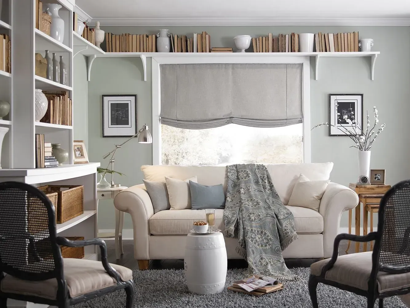 Living room with sofa, bookshelves, chairs, and books. Light green walls, rug, and white trim.