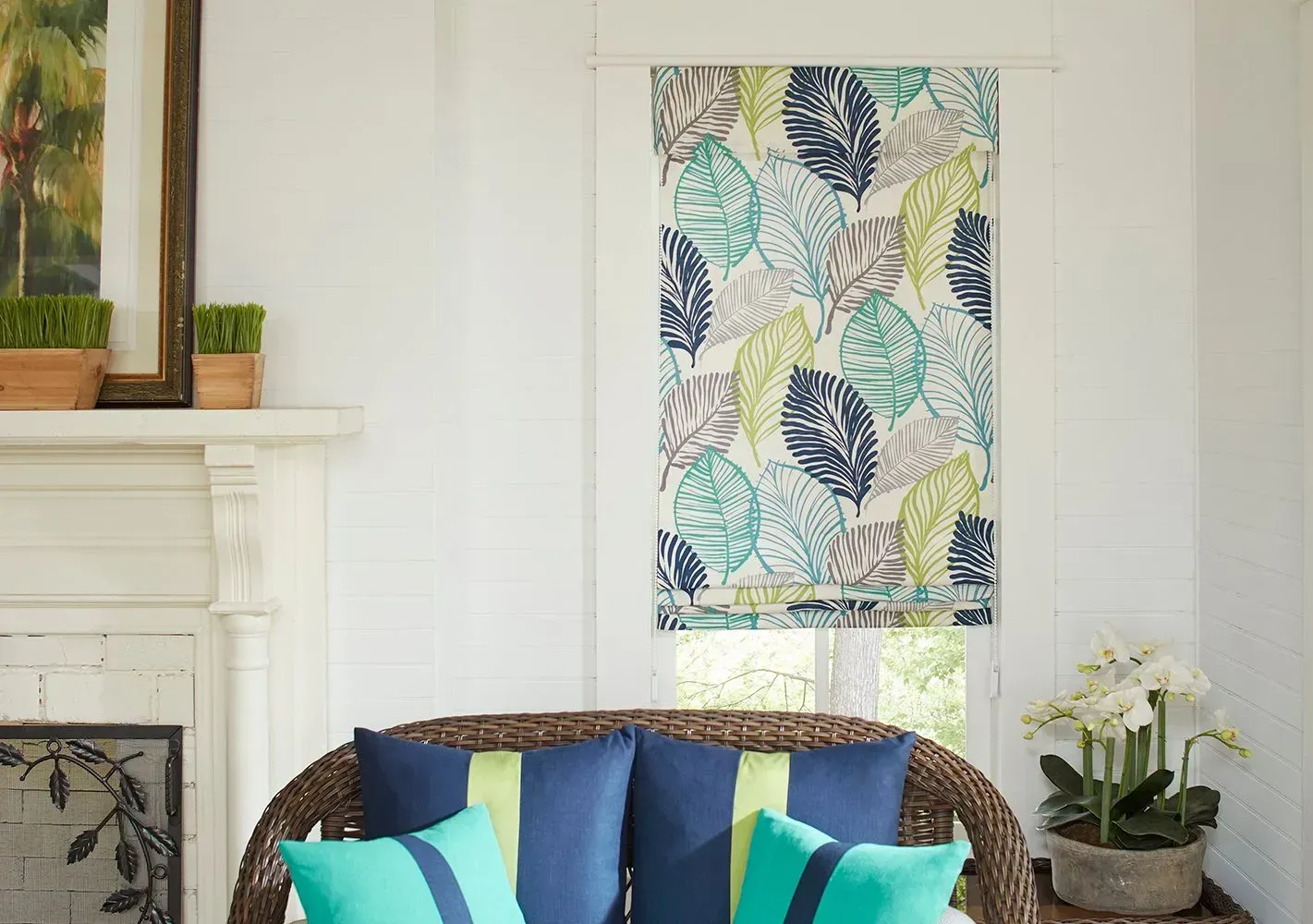 Room with floral patterned window shade, wicker loveseat with blue and green pillows, and a fireplace.