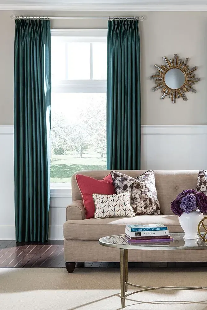 Living room with teal curtains, beige sofa, round coffee table, and sunburst mirror.