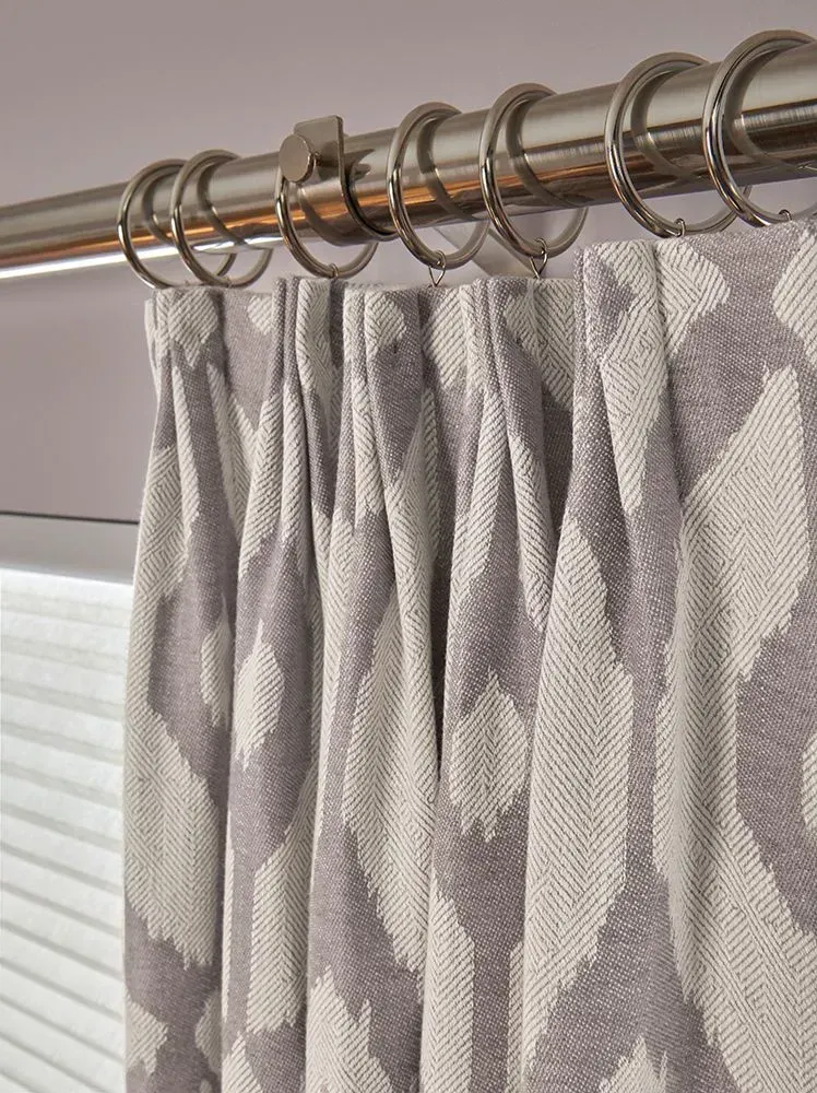 Close-up of pleated gray and white patterned curtain hanging from silver rings on a rod.