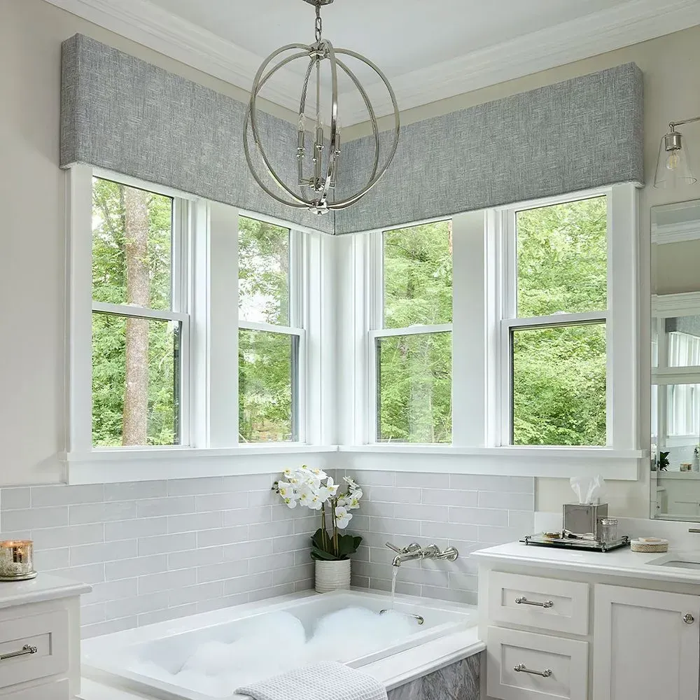 Bathroom corner with windows, tub, and silver orb chandelier. White cabinets, gray tile, and a forest view.