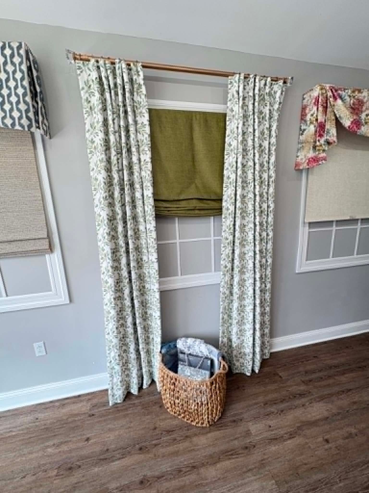 Curtained window nook with woven basket on wood floor and floral valances in a gray room