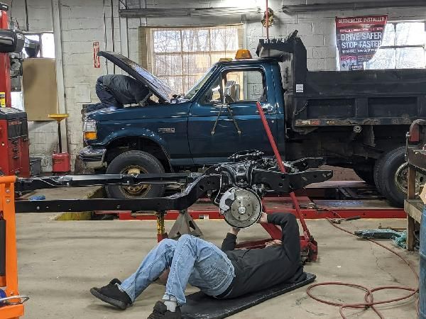 A man is laying on the floor working on a truck in a garage