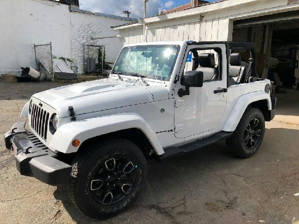 A white jeep is parked in front of a garage.