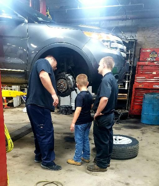 Three men and a boy are standing in front of a car in a garage.