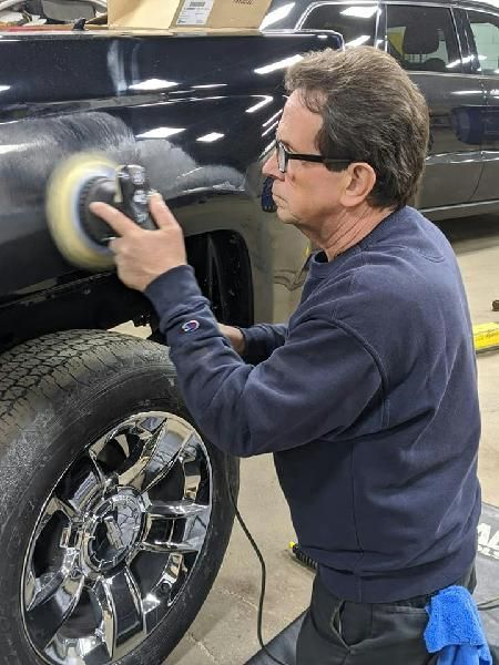A technician is polishing the fender of a truck.