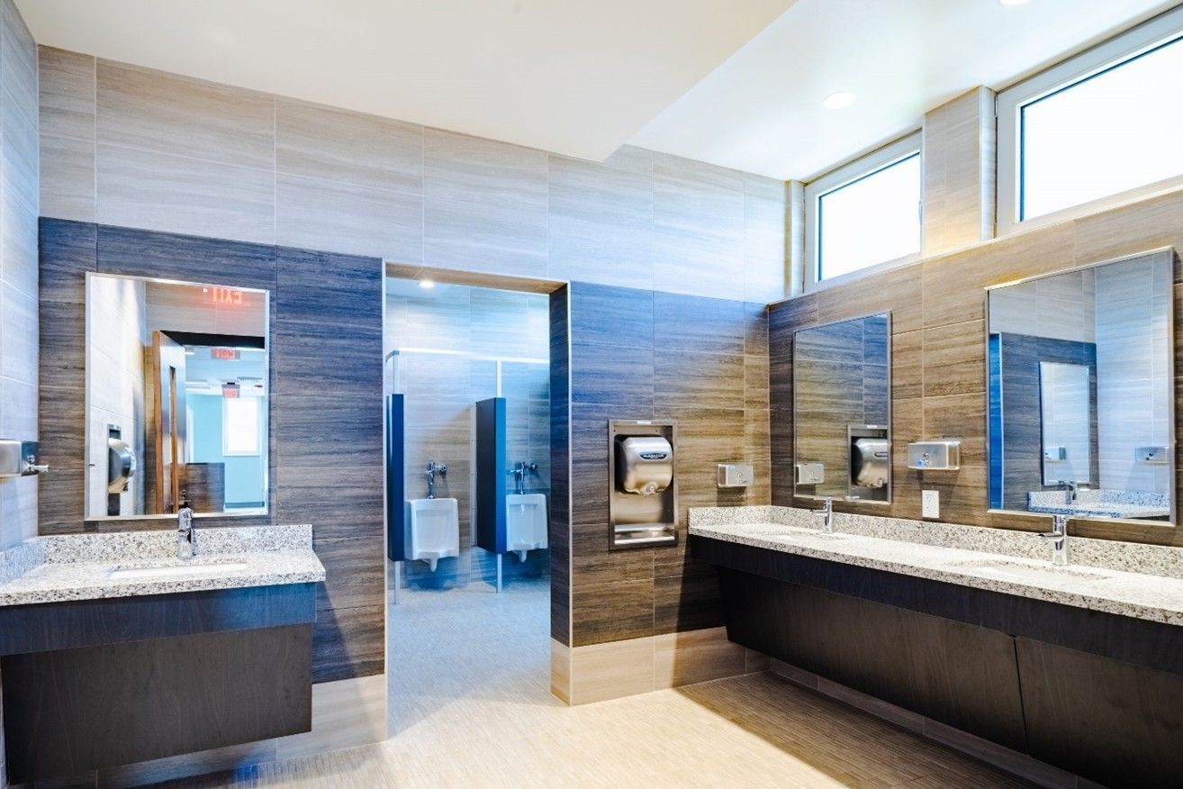 Modern public restroom with gray tiled walls, granite countertops, and stainless steel fixtures.