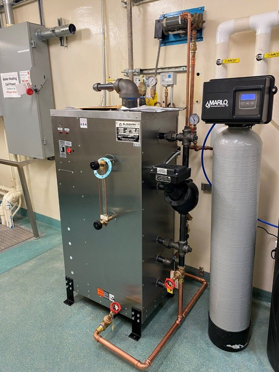 A stainless steel boiler with pipes and a water softener in a utility room.