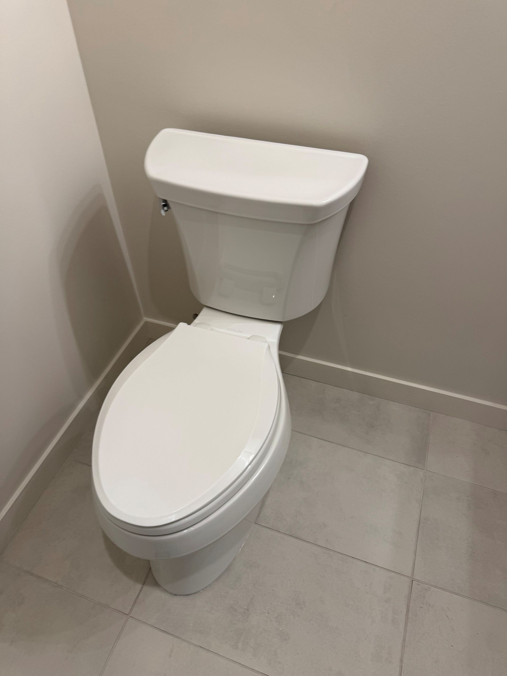White toilet in a bathroom, against a beige wall, and white tiled floor.