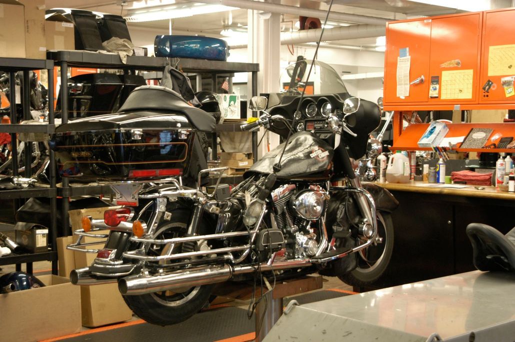 A black touring motorcycle is suspended on a lift in a brightly lit automotive workshop.