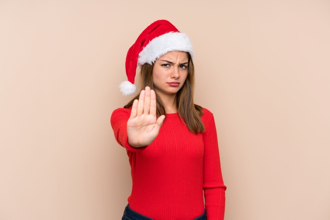 Woman in a Santa hat holding up a stop hand gesture against a beige background