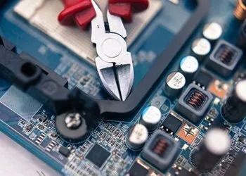 Pliers working on a blue computer circuit board with chips and components