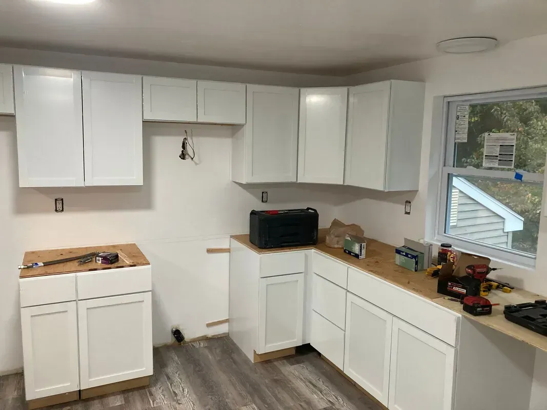 Kitchen under construction with white cabinets, wood countertops, and a window.