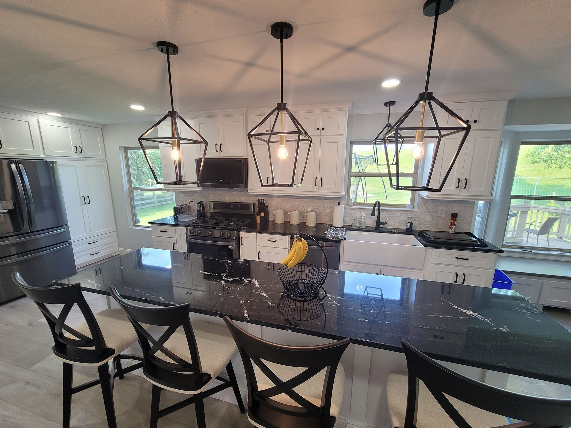 Modern kitchen with black island, white cabinets, and black geometric pendant lights.