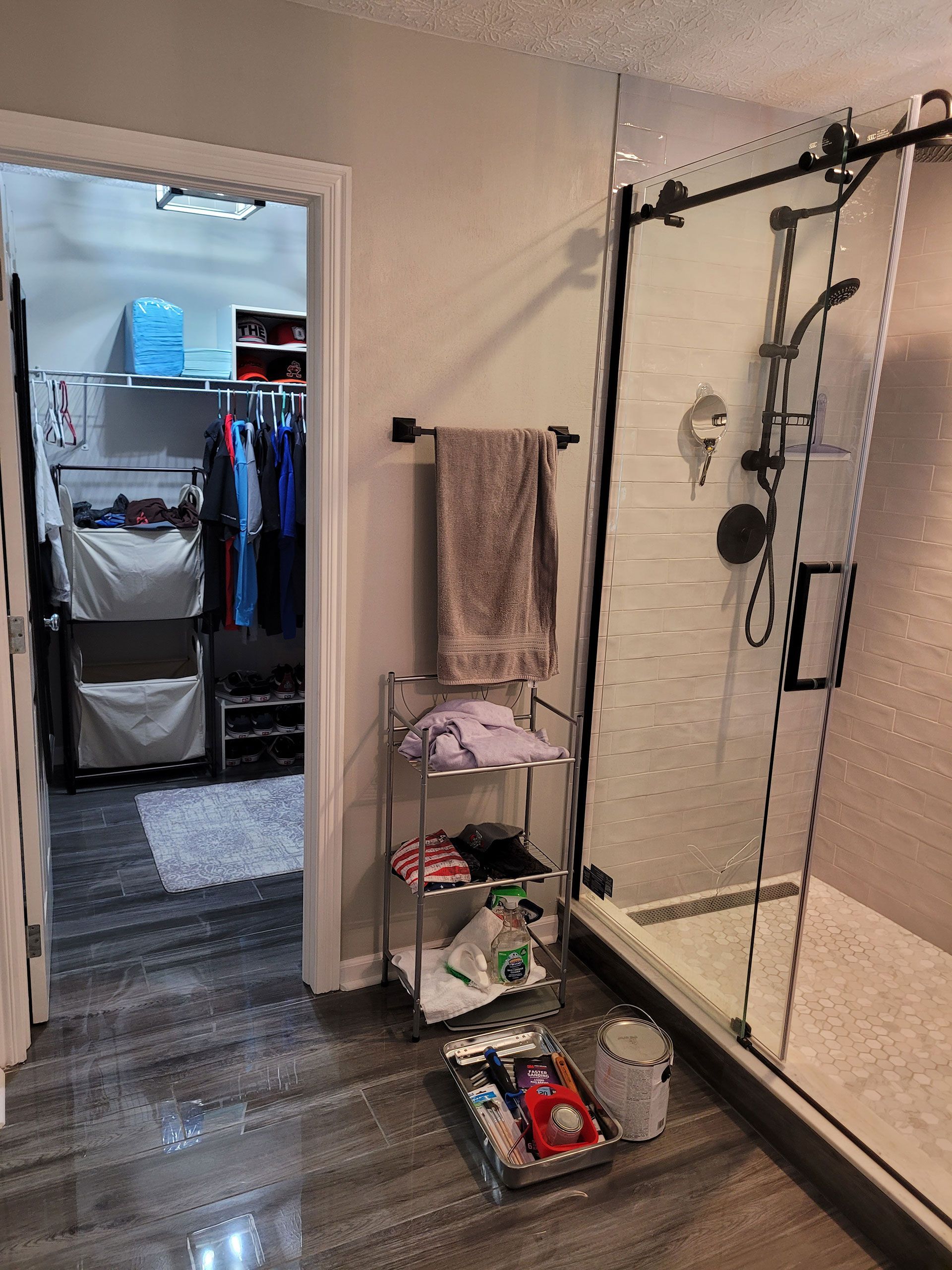 Bathroom with shower, shelving unit, and closet visible. Dark gray floors, white walls.