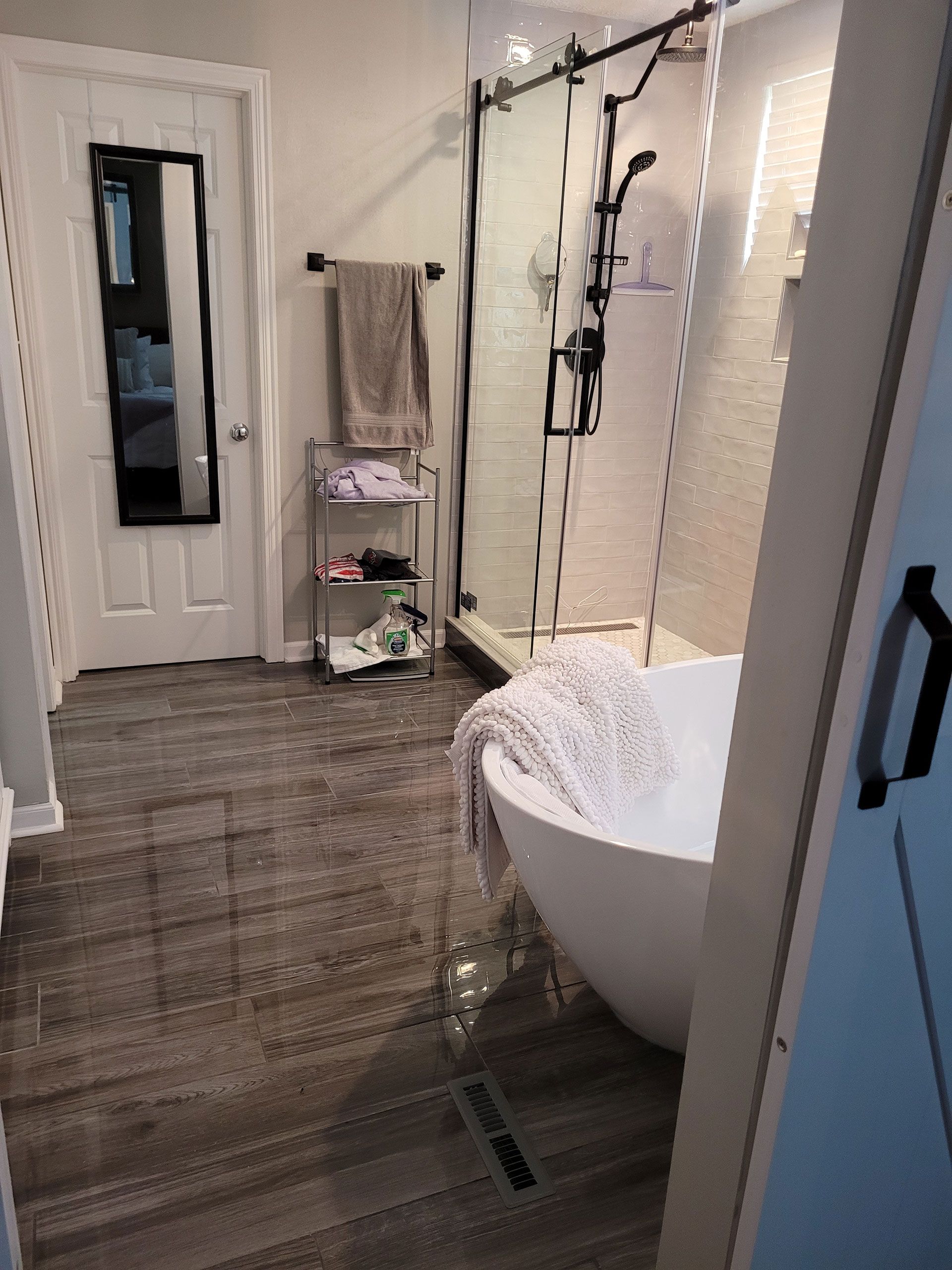 Bathroom with a modern tub, glass shower, towel rack, and dark wood-look floor.