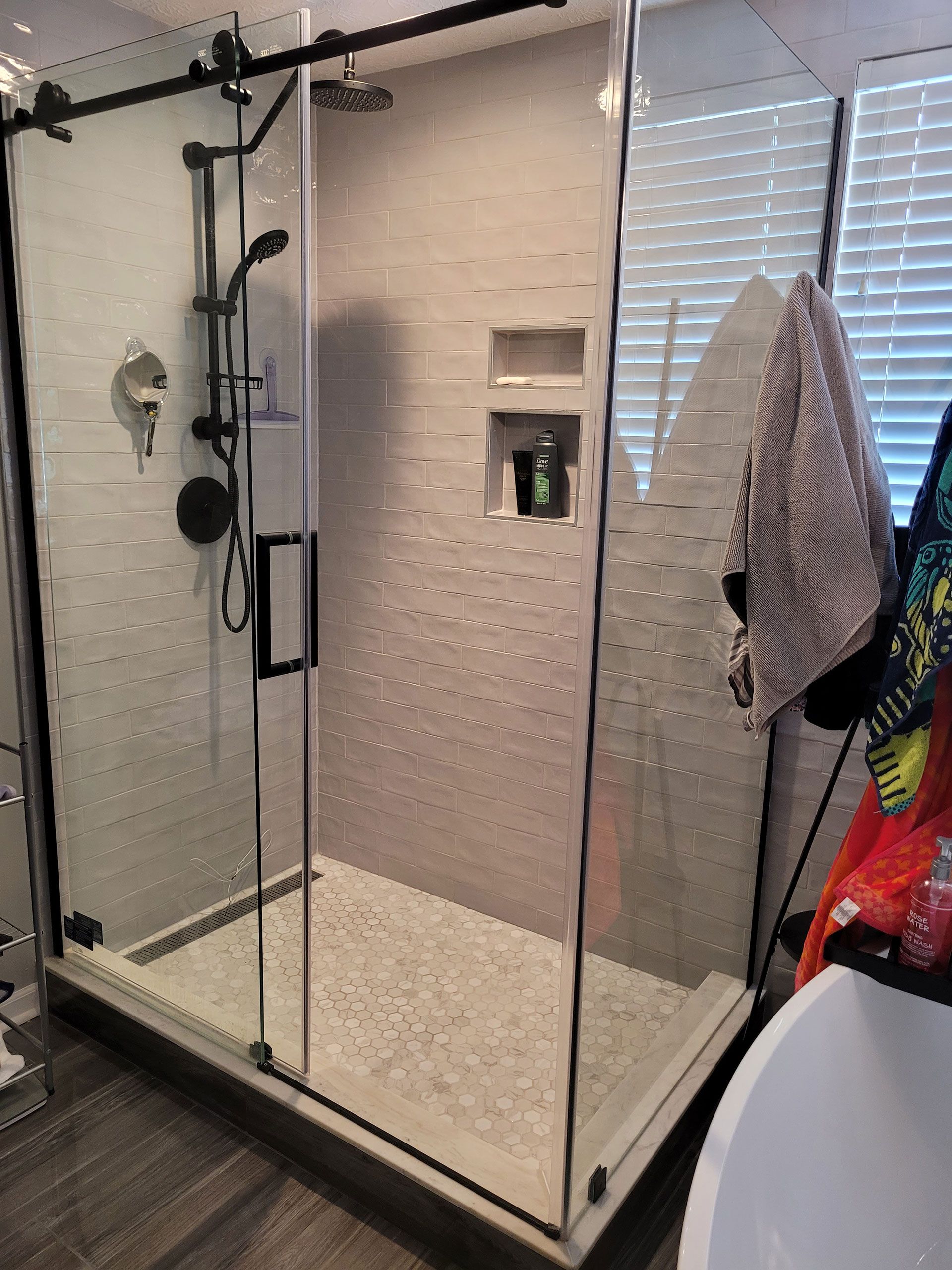 Modern shower with glass door, black fixtures, and mosaic floor tile.