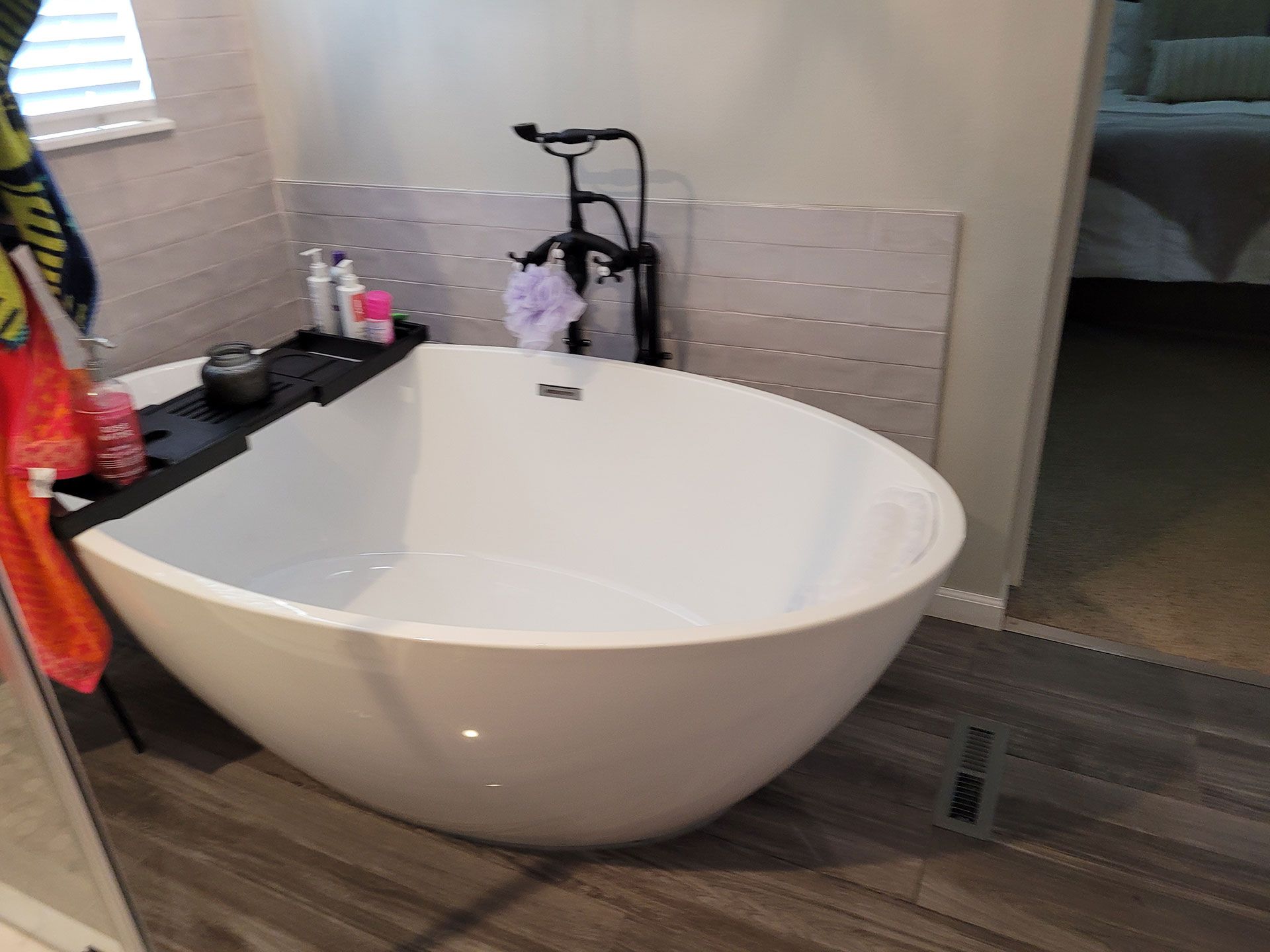 White oval bathtub with black faucet, tray, and towels in a bathroom.