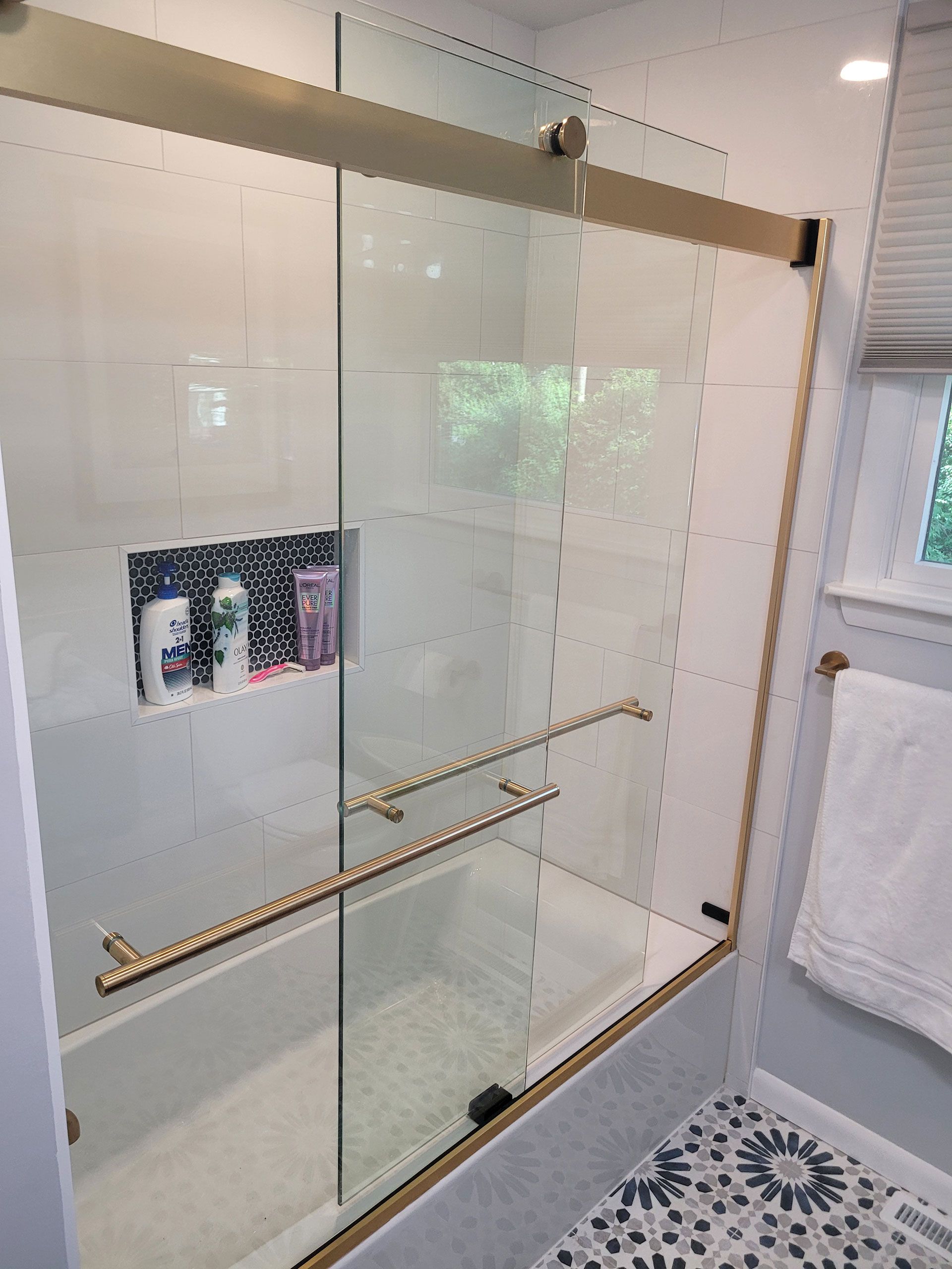 Bathroom with a glass shower door and gold trim, white tiles, and a built-in shelf.
