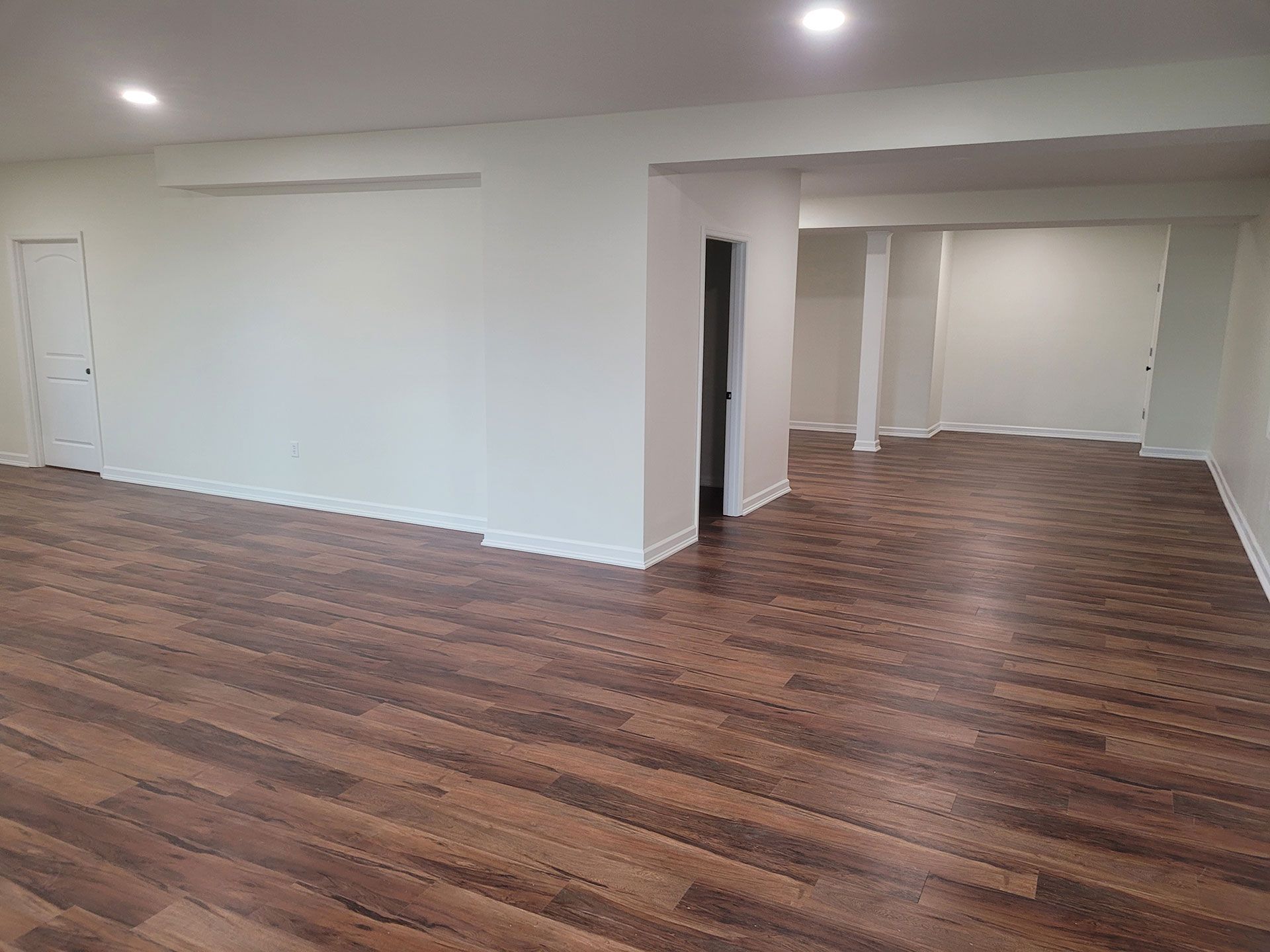 Empty room with dark wood-look flooring, white walls, and recessed lighting. Doorway to another room.