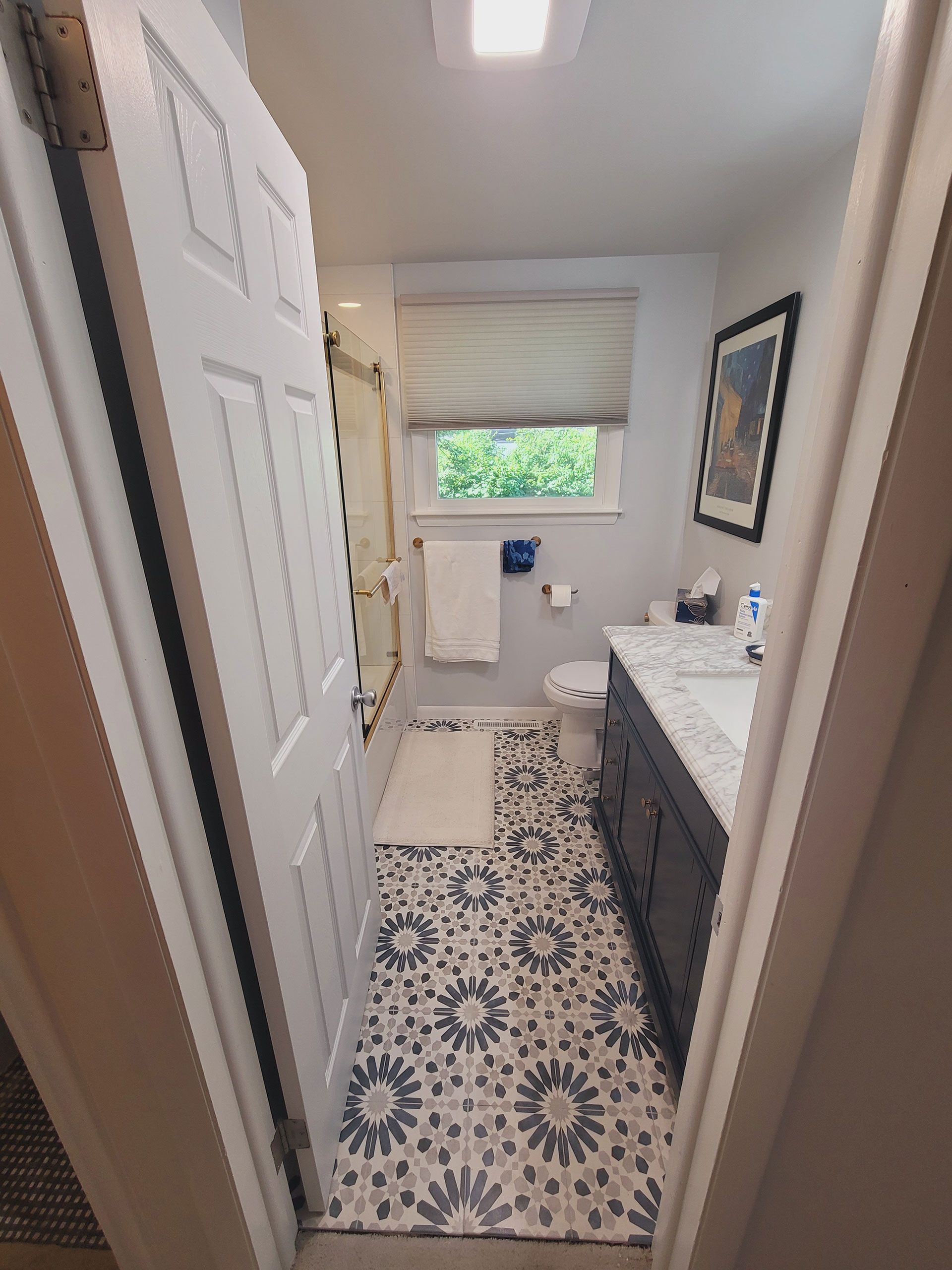Small bathroom with patterned floor, dark vanity, white door, and a window with a shade.