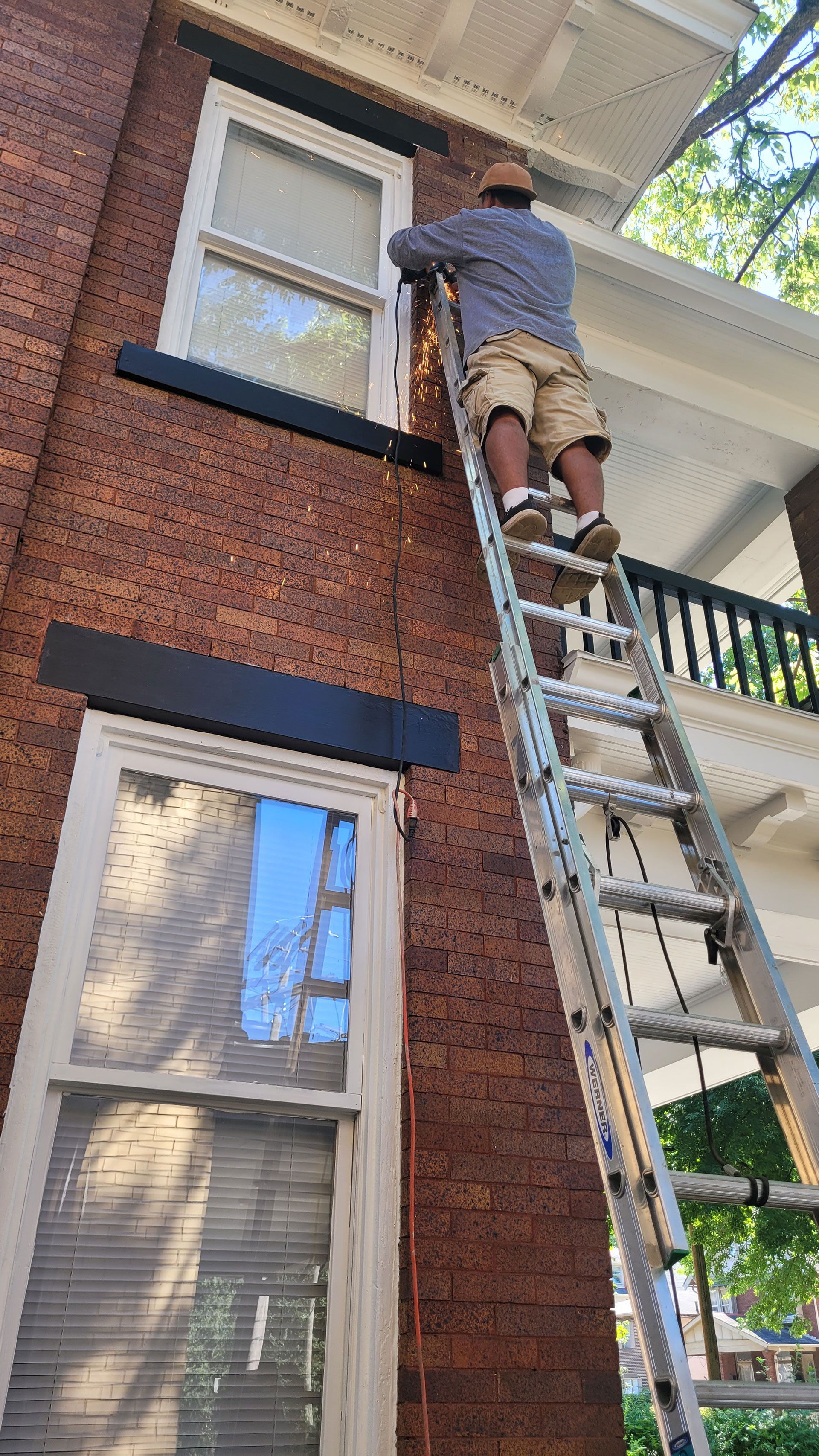 Person on ladder near brick building, installing something. Windows and balcony visible.