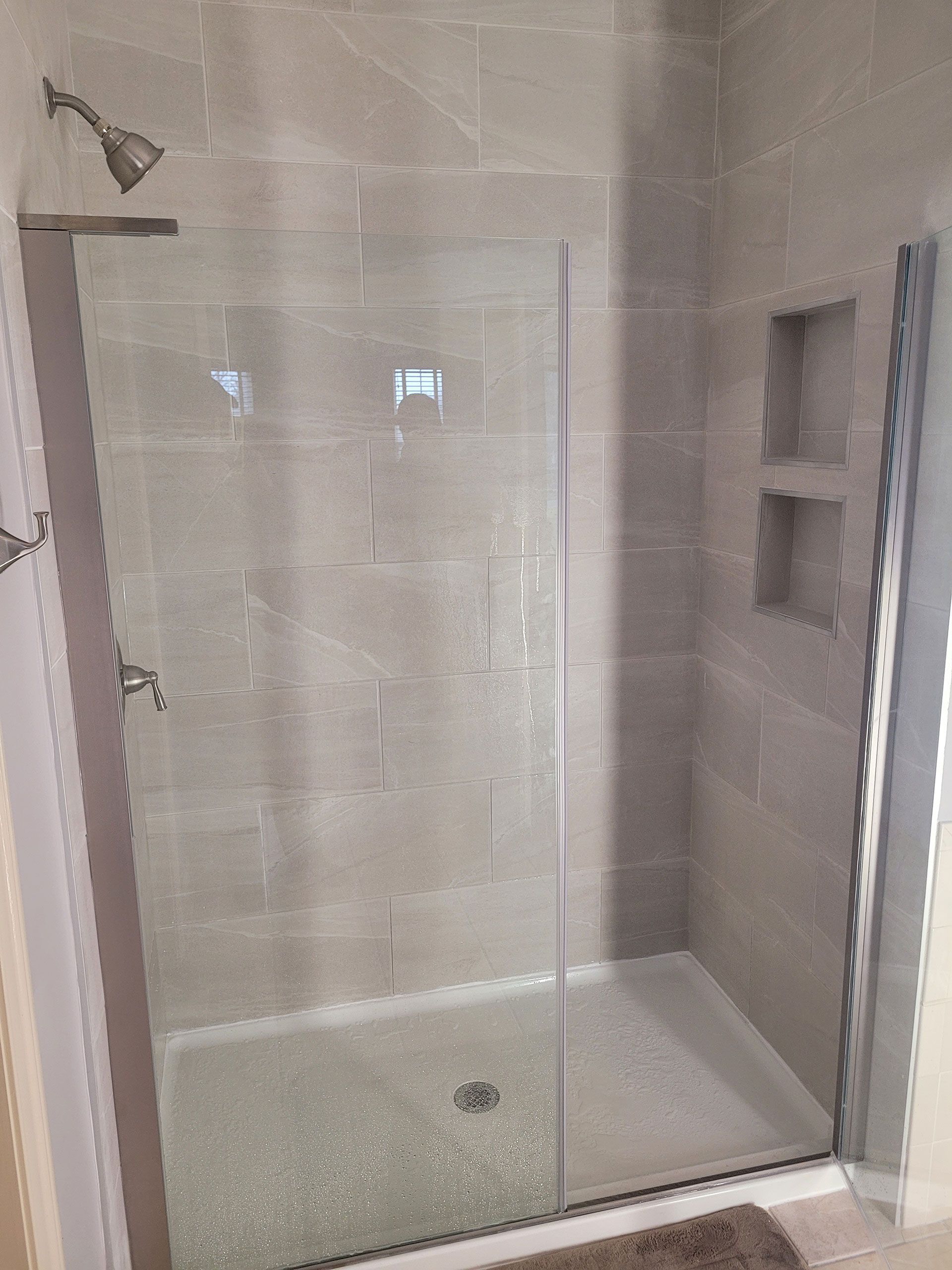 Shower stall with gray tile, glass door, and built-in shelves.
