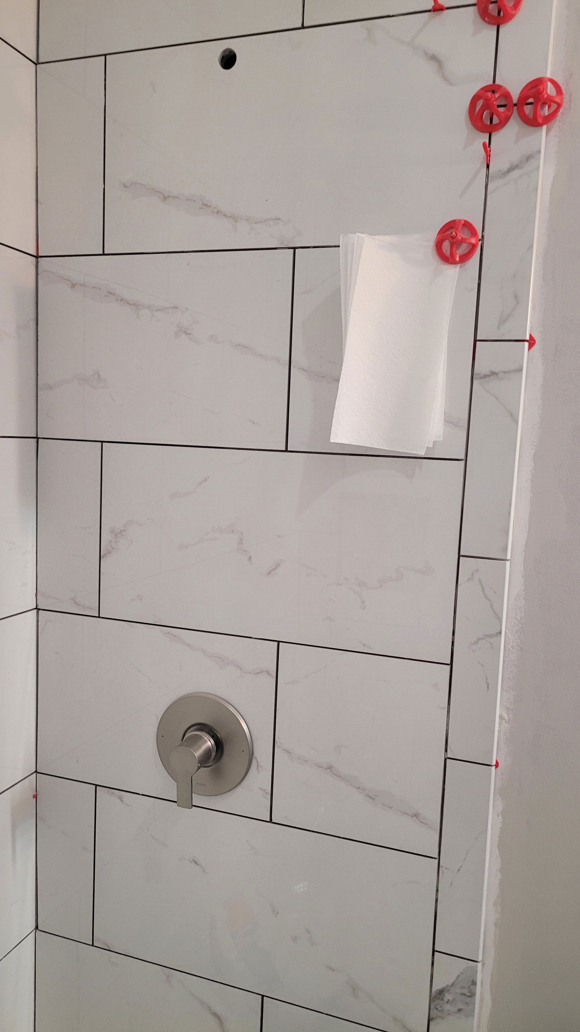 White tiled shower with built-in shelf and shower faucet. Tile spacers in use.