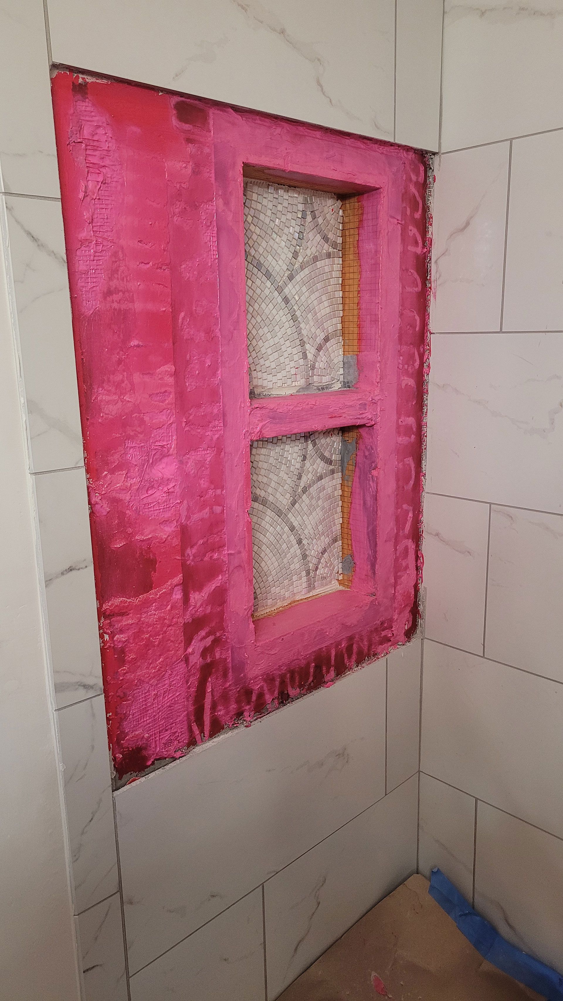 Pink shower niche frame built into tiled wall.