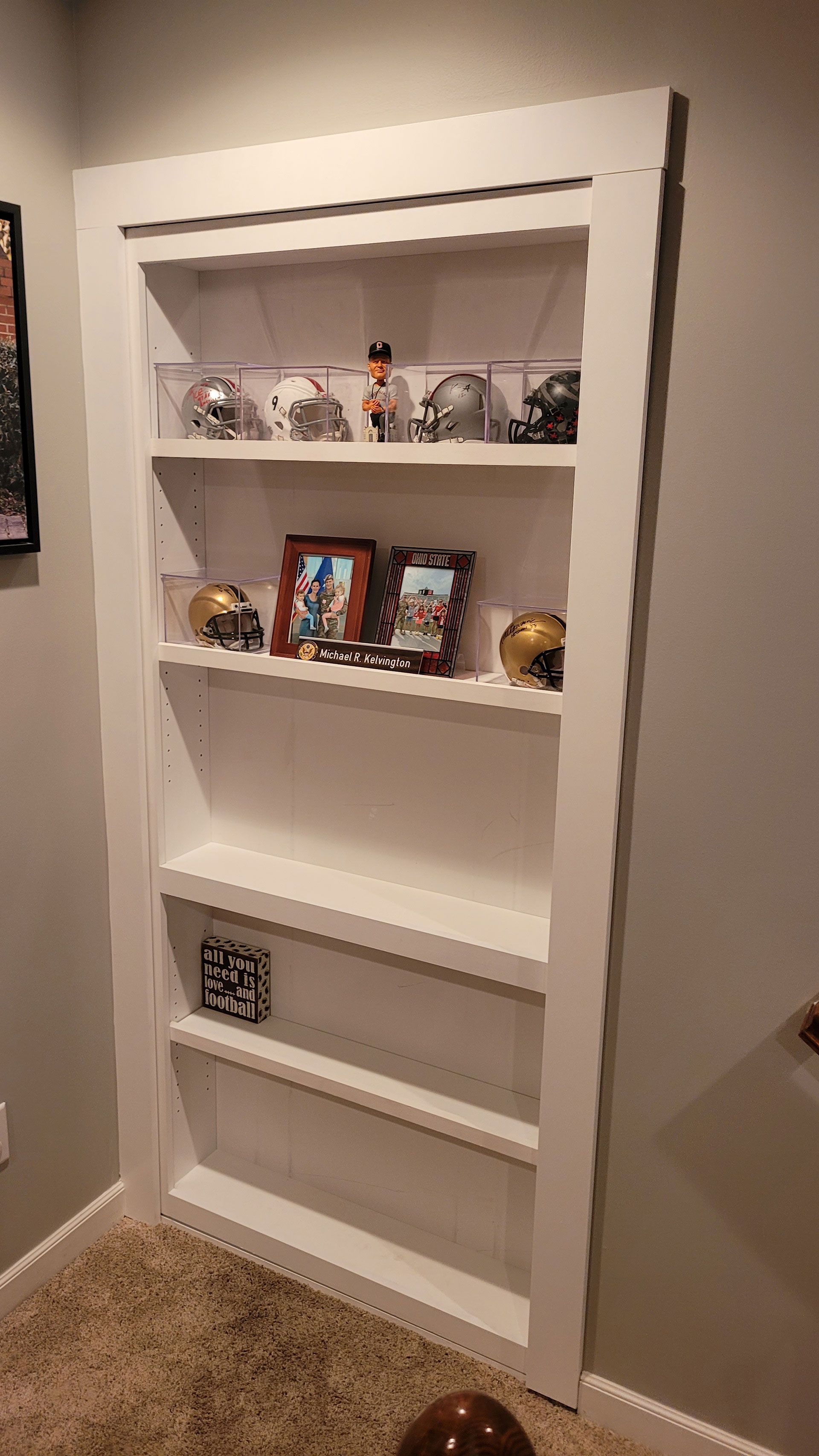 Built-in white shelves in a wall niche display sports memorabilia, including helmets and photos, against a neutral-colored wall.