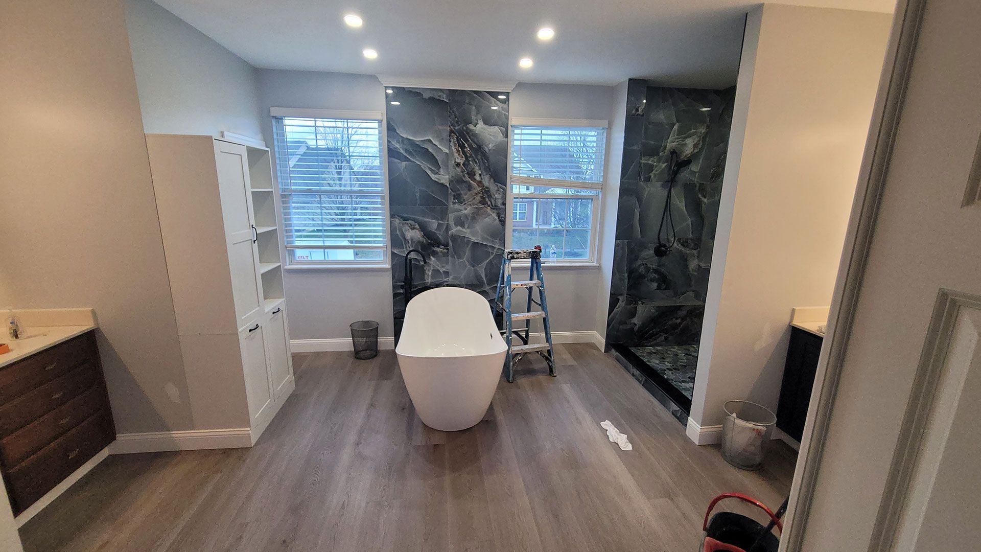 Bathroom with marble accent wall, two sinks, toilet, and a standing shower.