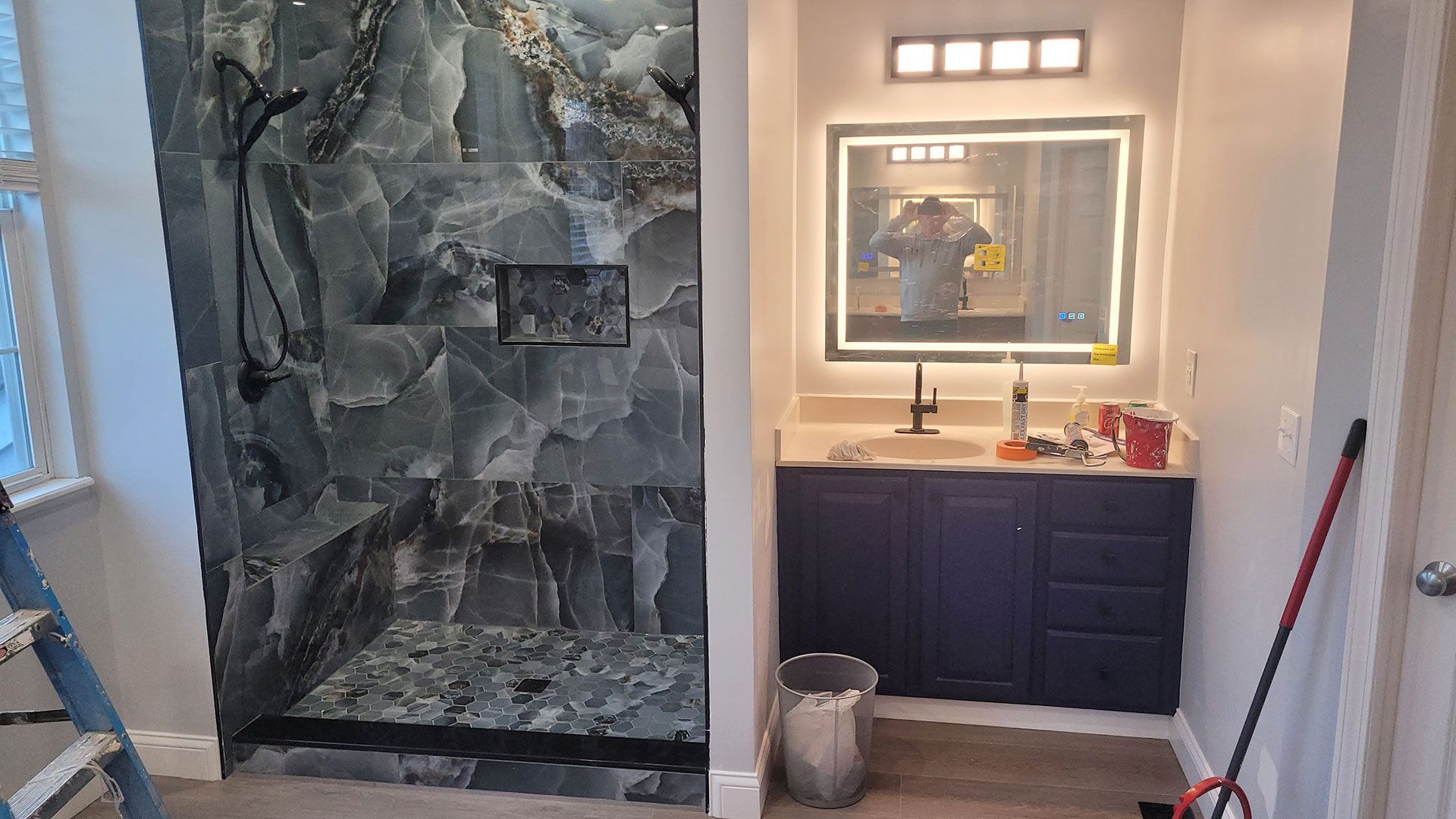 Bathroom with a marble-tiled shower and dark blue vanity with an illuminated mirror.