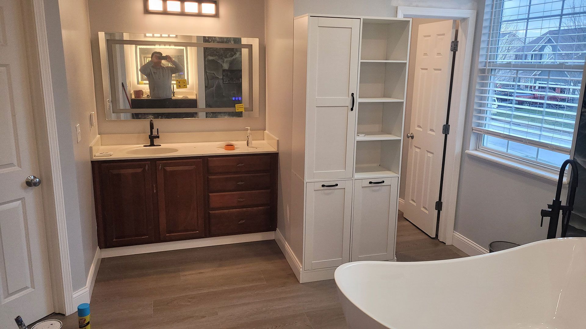 Bathroom with dark wood vanity, white storage cabinet, and window with blinds.