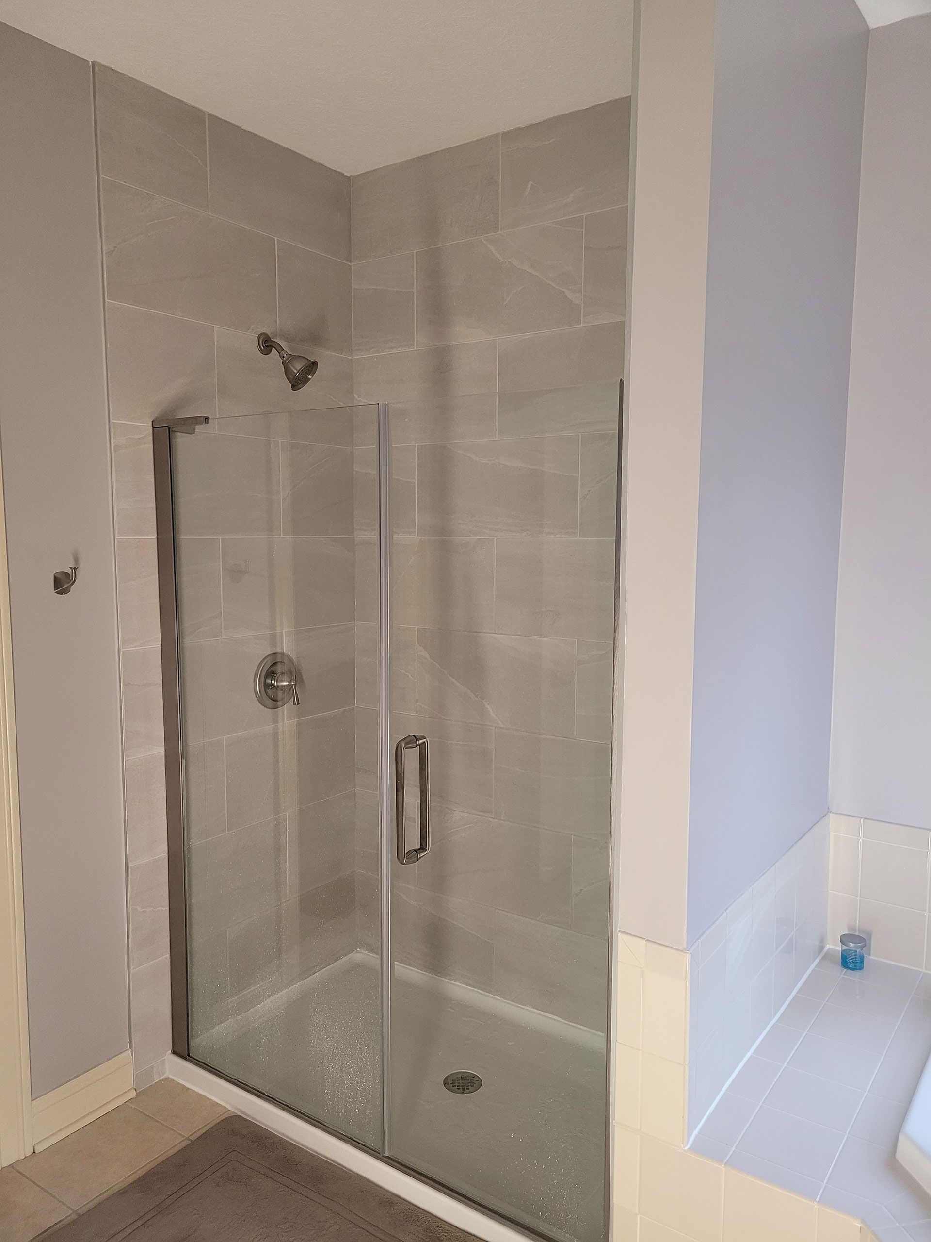 Gray-tiled shower with glass door and silver fixtures. Set in a bathroom with pale gray walls.