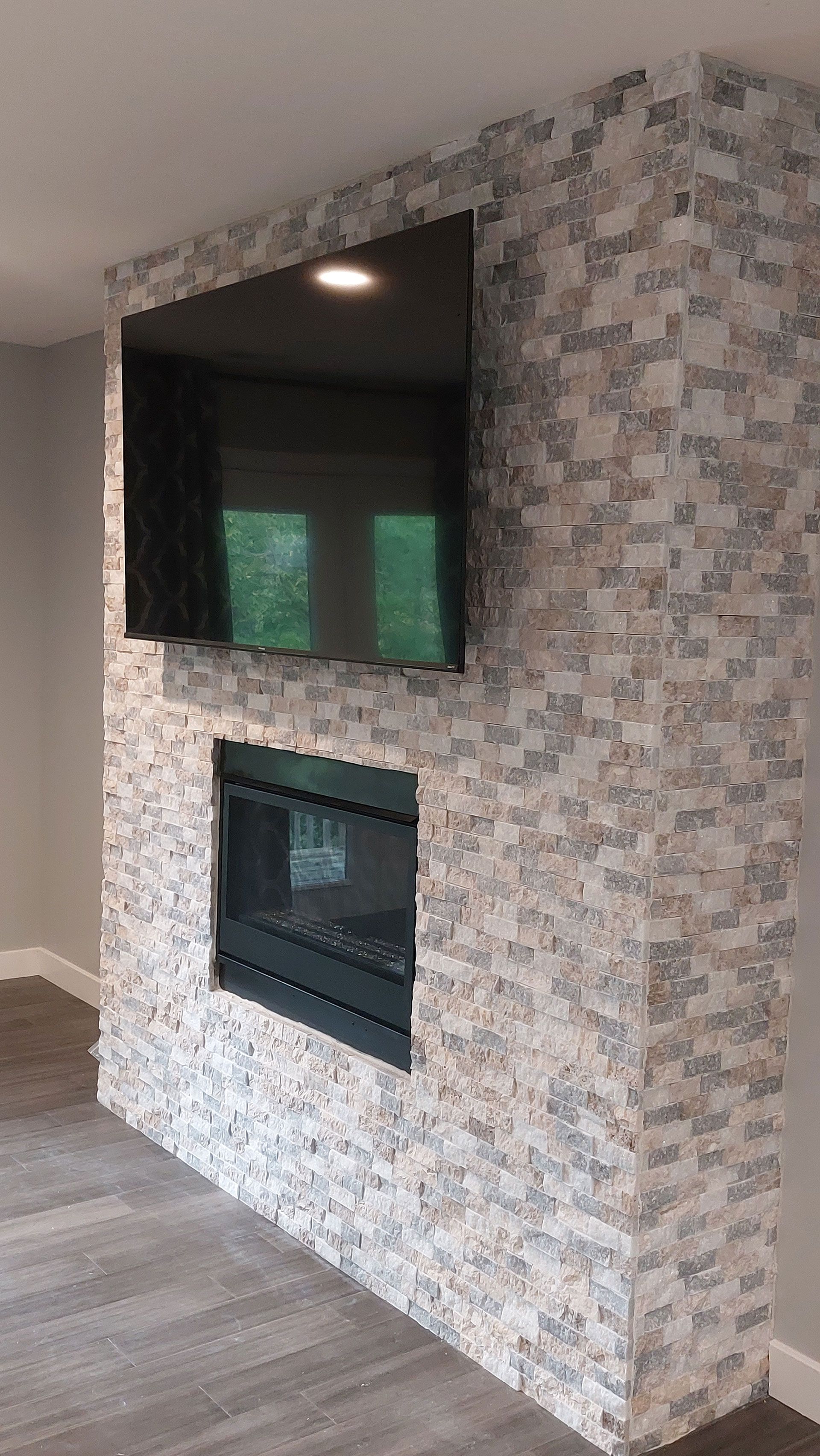 Fireplace with a built-in TV. Stone facade, black fireplace, large screen TV. Neutral colors.
