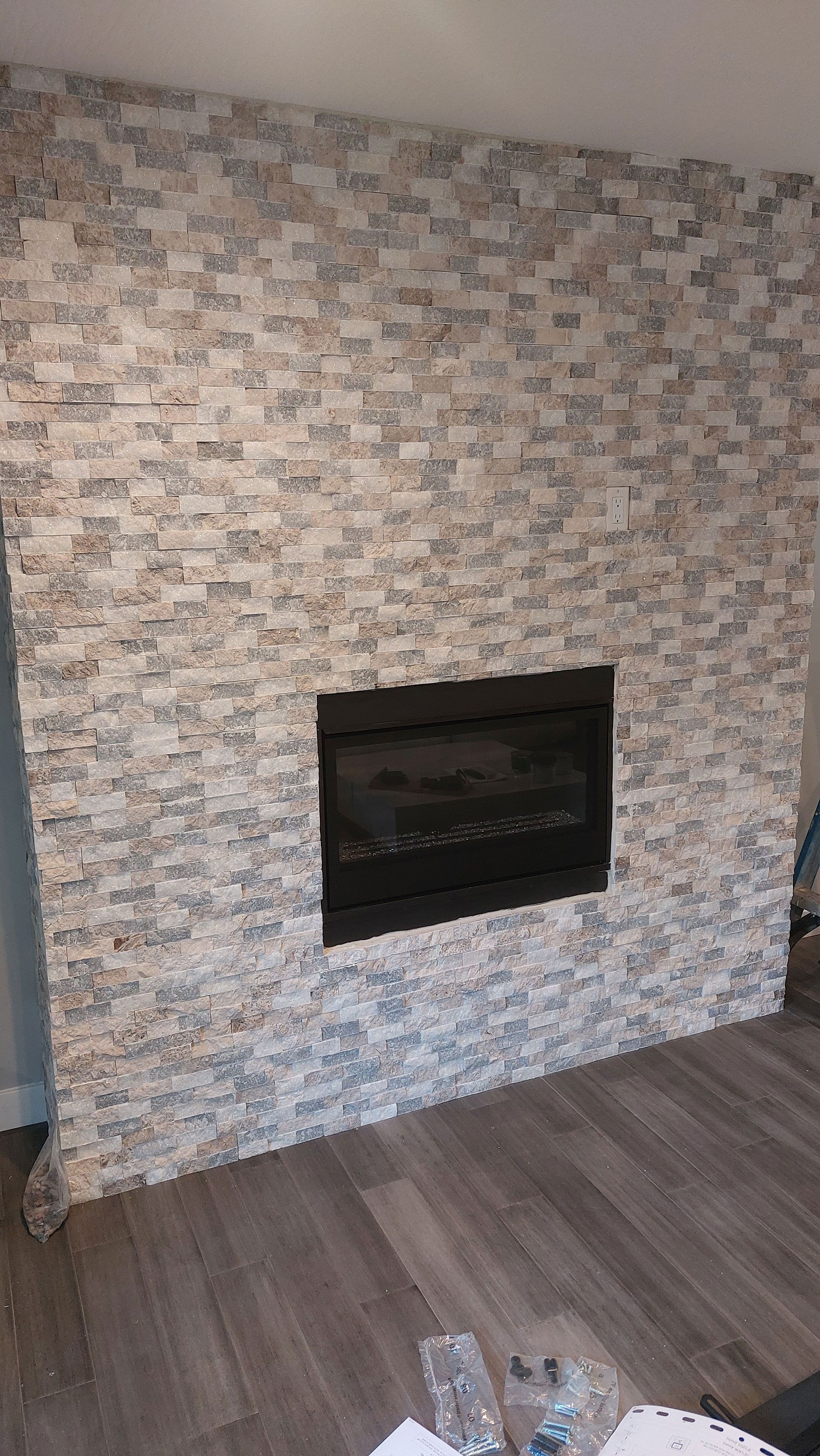 Fireplace with black insert framed by stone-look tiles, set against a wall, with wood-look flooring.